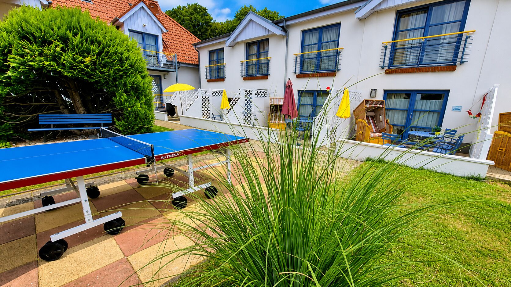 Une cour avec une table de ping-pong, des sièges extérieurs et un bâtiment blanc aux fenêtres bleues.