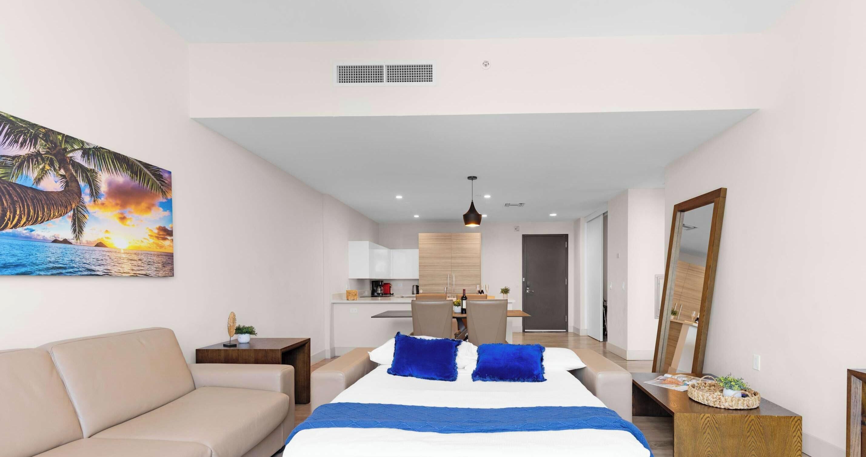 A hotel room with a bed, a sofa, a desk, and a kitchenette.