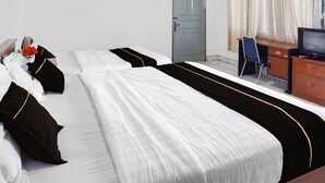 Una cama doble con ropa de cama blanco y negro, un aparador de madera, un televisor y una silla azul en una habitación de hotel.