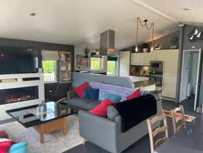 Ein modernes Wohnzimmer mit Kamin, einer Couch mit bunten Kissen, einem Essbereich mit Stühlen und einer Küche mit Mikrowelle.