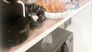 Een keukenhoek met een koffieapparaat, theekopjes, een mand met brood en een waterdispenser.