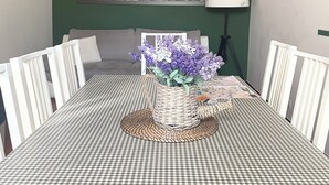 Een eethoek met een geruit tafelkleed, een rieten mand met bloemen, een schilderij van een fiets aan de muur, en een klok.