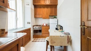 Een kleine keuken met houten kastjes, een fornuis en een tafel met een tafelkleed.