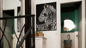 A staircase with a metal railing, a white cabinet with baskets, a zebra artwork, a green door, and a sink with a mirror.