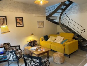 Un salón con un sofá amarillo, sillas estampadas de cebra, una mesa de centro y una escalera en espiral.