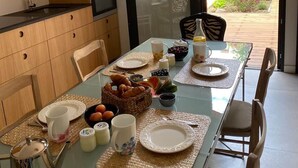 A modern kitchen with a dining area, a glass door leading to a garden, and a breakfast setup with various food items.