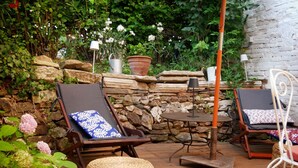 A patio with two lounge chairs, a small table, and a stone wall backdrop.
