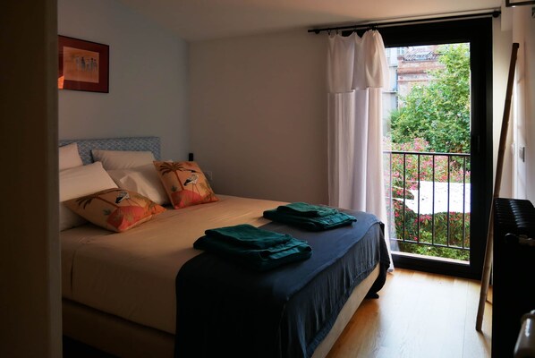 A bedroom with a bed, pillows, a window with a view of greenery, and a door to the right.