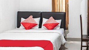 A bed with a white and red bedspread, two pillows with a red and white pattern, and a wooden chair to the right.