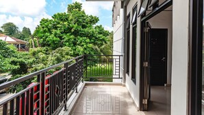 A balcony with a metal railing, a door, and a view of a green tree and a building in the background.