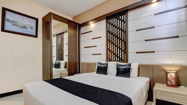 Habitación de hotel con una cama grande, cabecera de madera, mesita de noche, espejo y una lámpara fijada a la pared.