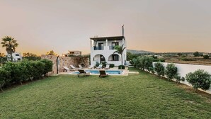 Ein modernes, zweistöckiges Haus mit Swimmingpool, umgeben von einem gepflegten Rasen und Palmen.