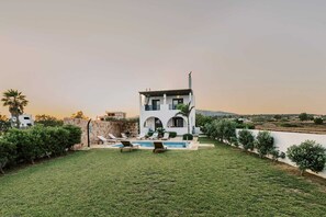 Ein modernes, zweistöckiges Haus mit Swimmingpool, umgeben von einem gepflegten Rasen und Palmen.