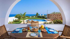 Ein Esstisch mit Tellern, Besteck und Gläsern mit Blick auf einen Swimmingpool und das Meer.