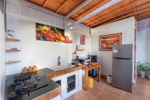 Une cuisine équipée d’une cuisinière, d’un évier, d’un réfrigérateur, de meubles de rangement en bois et d’un tableau représentant des fruits et des légumes accroché au mur.