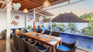 A covered outdoor dining area with wicker furniture, a wooden table, and a view of a swimming pool. - Nusa Sunshine Private Villa Ceningan (Ceningan Island)
