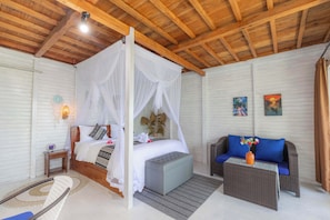 Une chambre à coucher avec un lit à baldaquin, un canapé, une petite table et une chaise en osier.