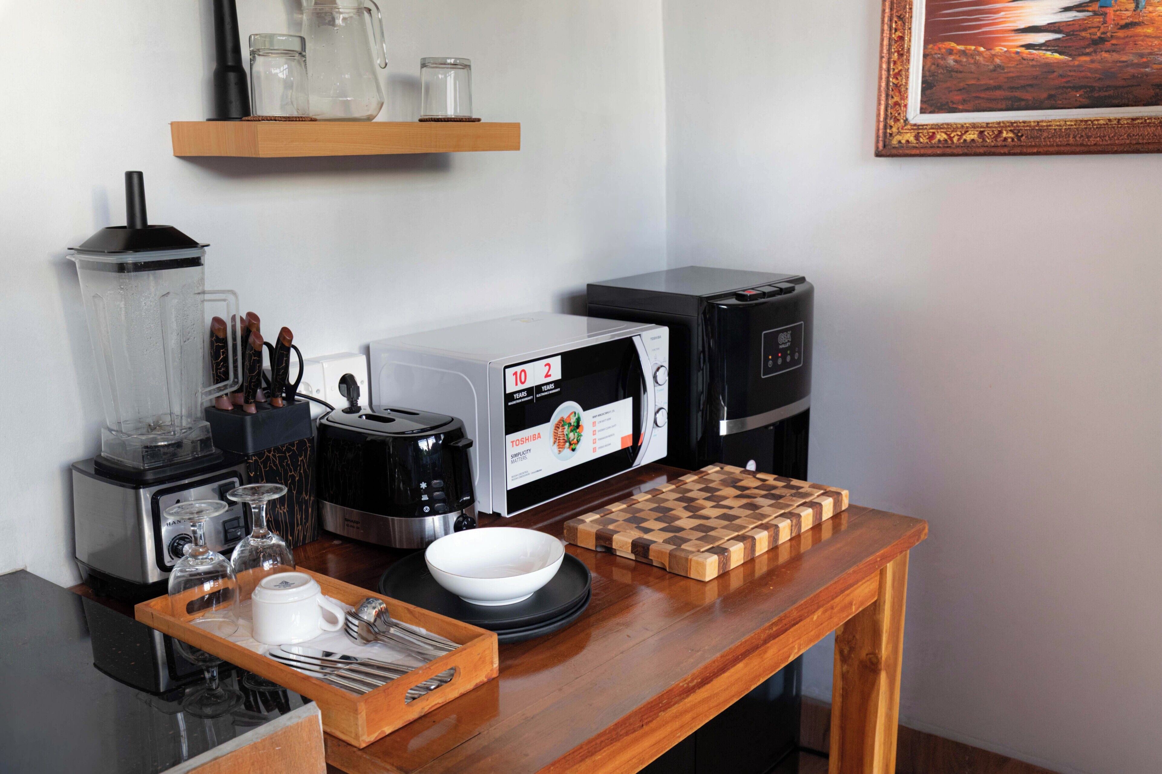 Una cocina con cafetera, tostadora, licuadora y tabla de cortar a cuadros sobre la encimera.