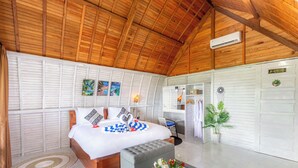 A bedroom with a wooden ceiling, a bed with a white and blue checkered blanket, a grey ottoman, a small table with a vase of flowers, and a white wardrobe. - Nusa Sunshine Private Villa Ceningan (Ceningan Island)