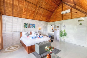 A bedroom with a wooden ceiling, a bed with a white and blue checkered blanket, a grey ottoman, a small table with a vase of flowers, and a white wardrobe. - Nusa Sunshine Private Villa Ceningan (Ceningan Island)