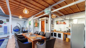 An open-plan living area with a dining table, wicker chairs, a ceiling fan, and a kitchen area with a refrigerator. - Nusa Sunshine Private Villa Ceningan (Ceningan Island)