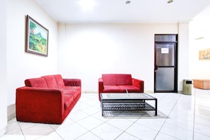 Ein Zimmer mit zwei roten Sofas, einem schwarzen Couchtisch, einer Tür mit Kühlschrank und einem gerahmten Bild an der Wand.