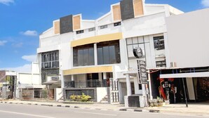 Un edificio moderno con una entrada amplia, un letrero visible que dice 'KANTIN' y una señalización de estacionamiento.
