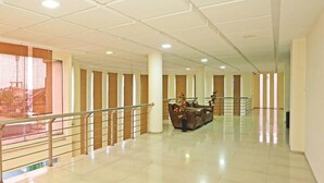 Eine großzügige Lobby mit hoher Decke, einer zentralen Sitzgruppe und einer Treppe mit Metallgeländer.