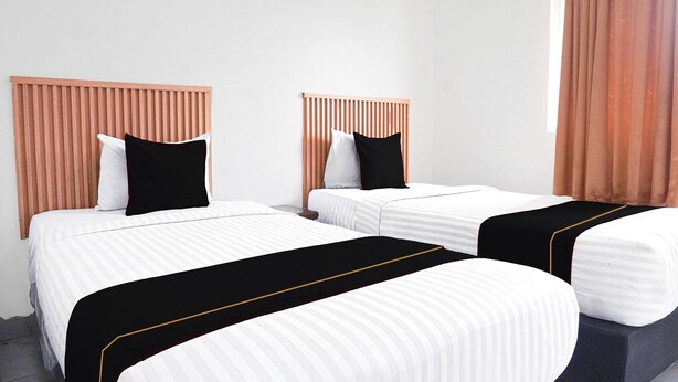 A hotel room with two beds, each with a wooden headboard, white bedding, and black and white pillows. - Cozy Twin Escape with Free WiFi and Parking (Padang)