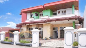 Una casa de dos pisos con techo rojo, paredes verdes y blancas, y una entrada protegida por una reja.