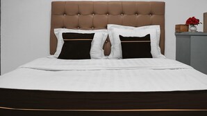 Una cama con cabecera acolchada, ropa de cama blanca y almohadas negras.
