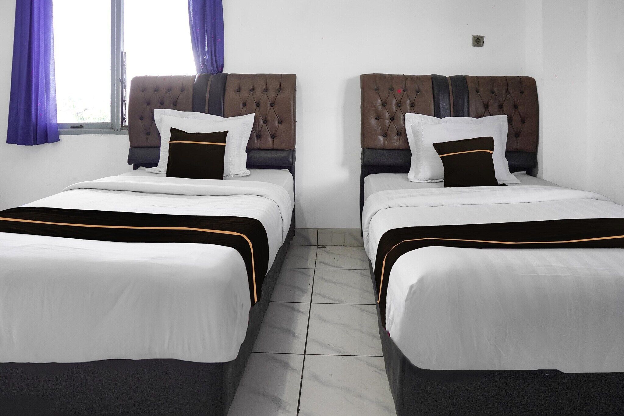 A hotel room with two beds, each with a tufted headboard, white bedding, and a black and gold accent.