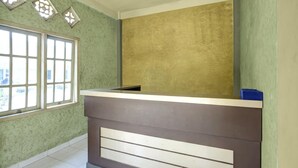 Un mostrador de recepción con ventanal, una pared con diseño texturizado y un techo con detalle decorativo.