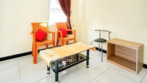 A room with two wooden chairs with red cushions, a small table with a patterned tablecloth, and a wooden cabinet.