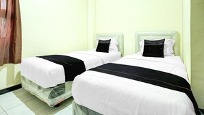 Two single beds with white and black bedding, a plain light-colored wall, and a brown curtain.