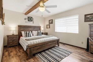 A bedroom with a wooden bed, a ceiling fan, a window with blinds, and a nightstand with a lamp. - Peaceful chalet, Bass Lake and Yosemite, hot-tub (Oakhurst)