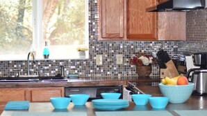 A kitchen with a tiled backsplash, wooden cabinets, a sink, and a fruit bowl on the counter. - Yosemite, River falls Retreat — Bass Lake (Oakhurst)