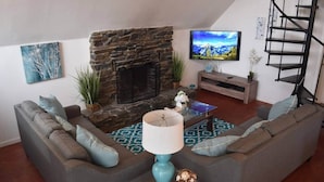 A living room with a stone fireplace, a sofa set, a coffee table, a TV, and a spiral staircase. - Yosemite, River falls Retreat — Bass Lake (Oakhurst)