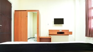 Ein Hotelzimmer mit einem Bett, einem Holzschrank, einem kleinen Nachttisch, einem an der Wand befestigten Fernseher und einer Tür zu einem weiteren Raum.