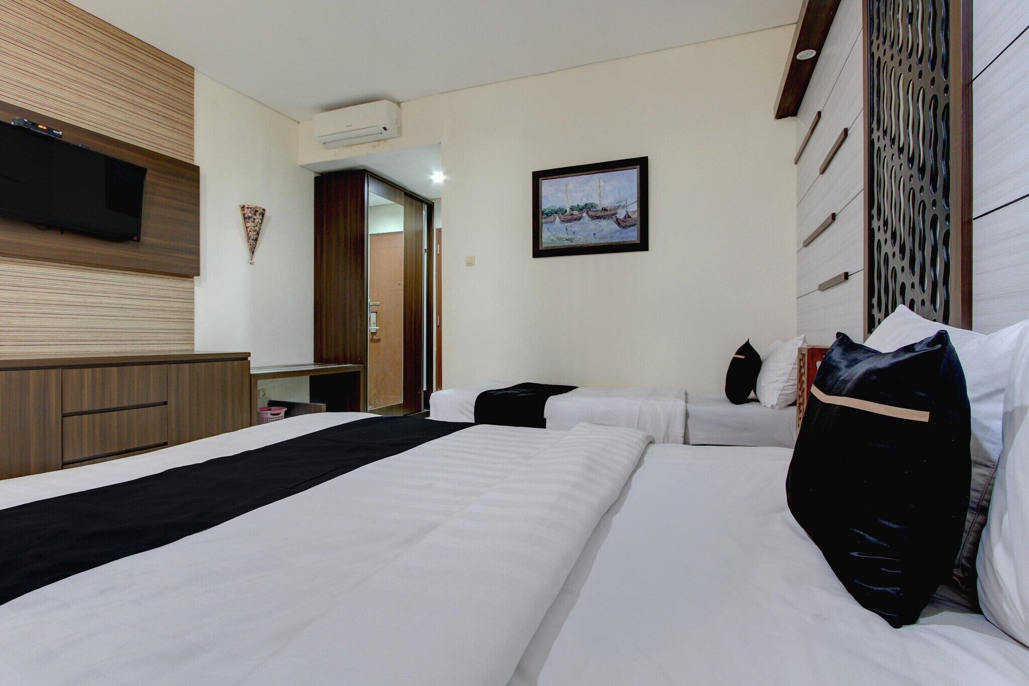 Habitación de hotel con dos camas, una televisión de pantalla plana, un cuadro y un cabecero de madera.