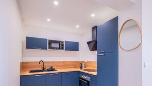 Eine kleine Küche mit blauen Schränken, einer Mikrowelle, einer Kaffeemaschine und einer Holzausziehtafel.