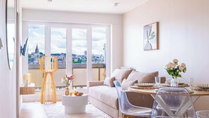 Ein modernes Wohnzimmer mit Sofa, Couchtisch und Esstisch, großen Fenstern mit Stadtblick und einem gerahmten Kunstwerk an der Wand.