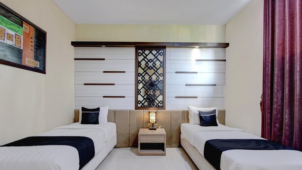 Een hotelkamer met twee bedden, een nachtkastje met een lamp, een decoratief paneel en een schilderij aan de muur.