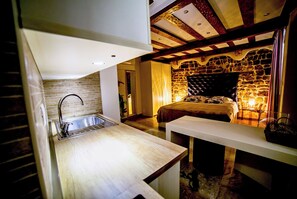 Quarto compacto com cozinha compacta, uma cama e uma parede de pedra, além de teto de madeira.