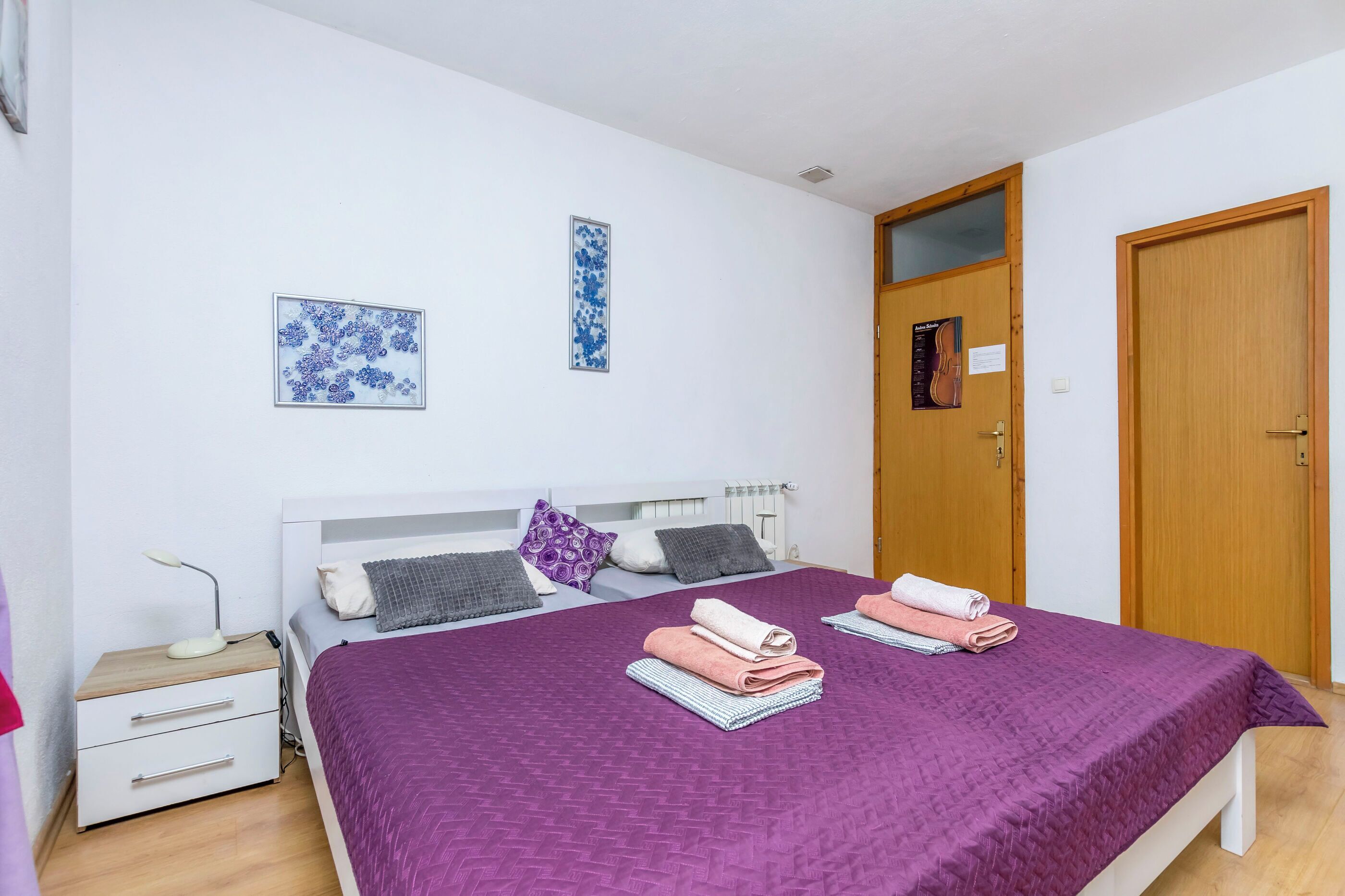 A bedroom with a bed, two pillows, a nightstand, a lamp, and two towels.