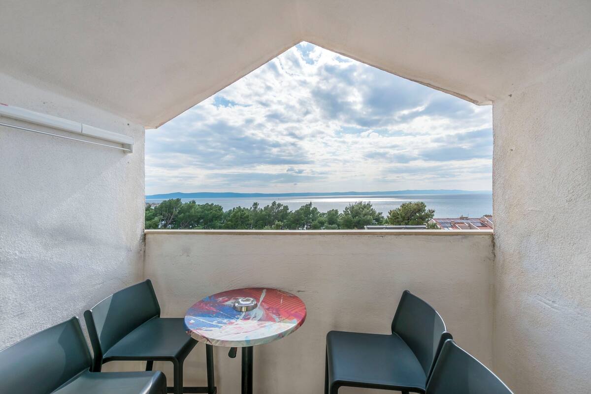 A balcony with a table and chairs, a view of the sea, and a clear sky.
