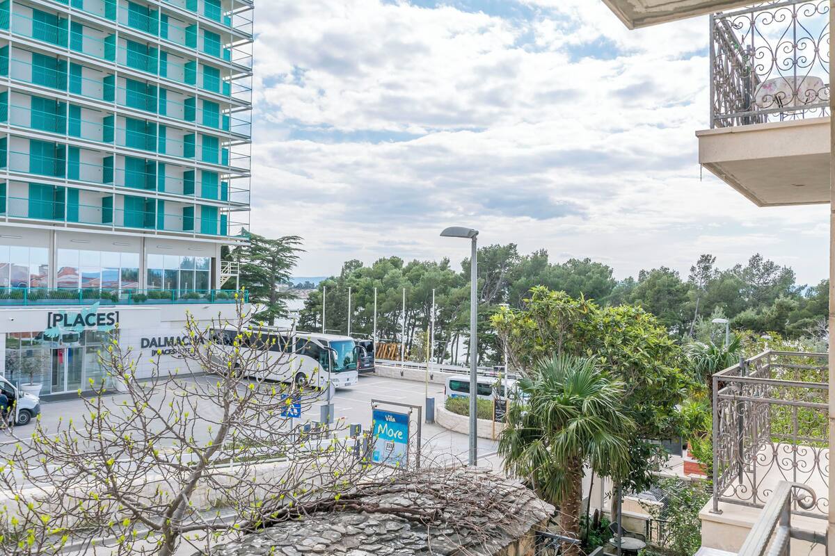 A multi-story building with a modern design, a parking area with buses, and a view of a green landscape.