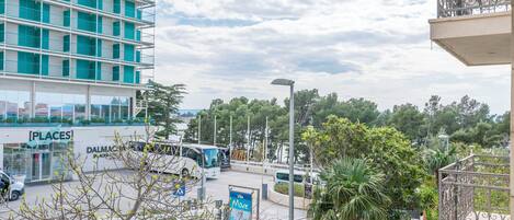 A multi-story building with a modern design, a parking area with buses, and a view of a green landscape.