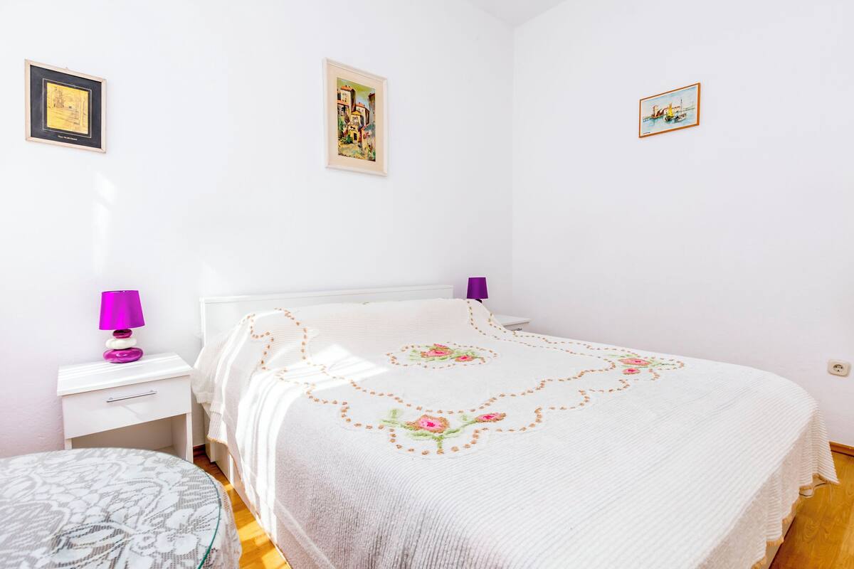 A bedroom with a bed, a bedside table, a lamp, and a small chair.
