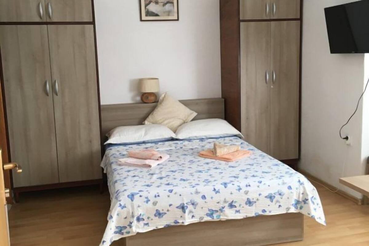 A bedroom with a bed, two wardrobes, a bedside table with a lamp, and a TV mounted on the wall.